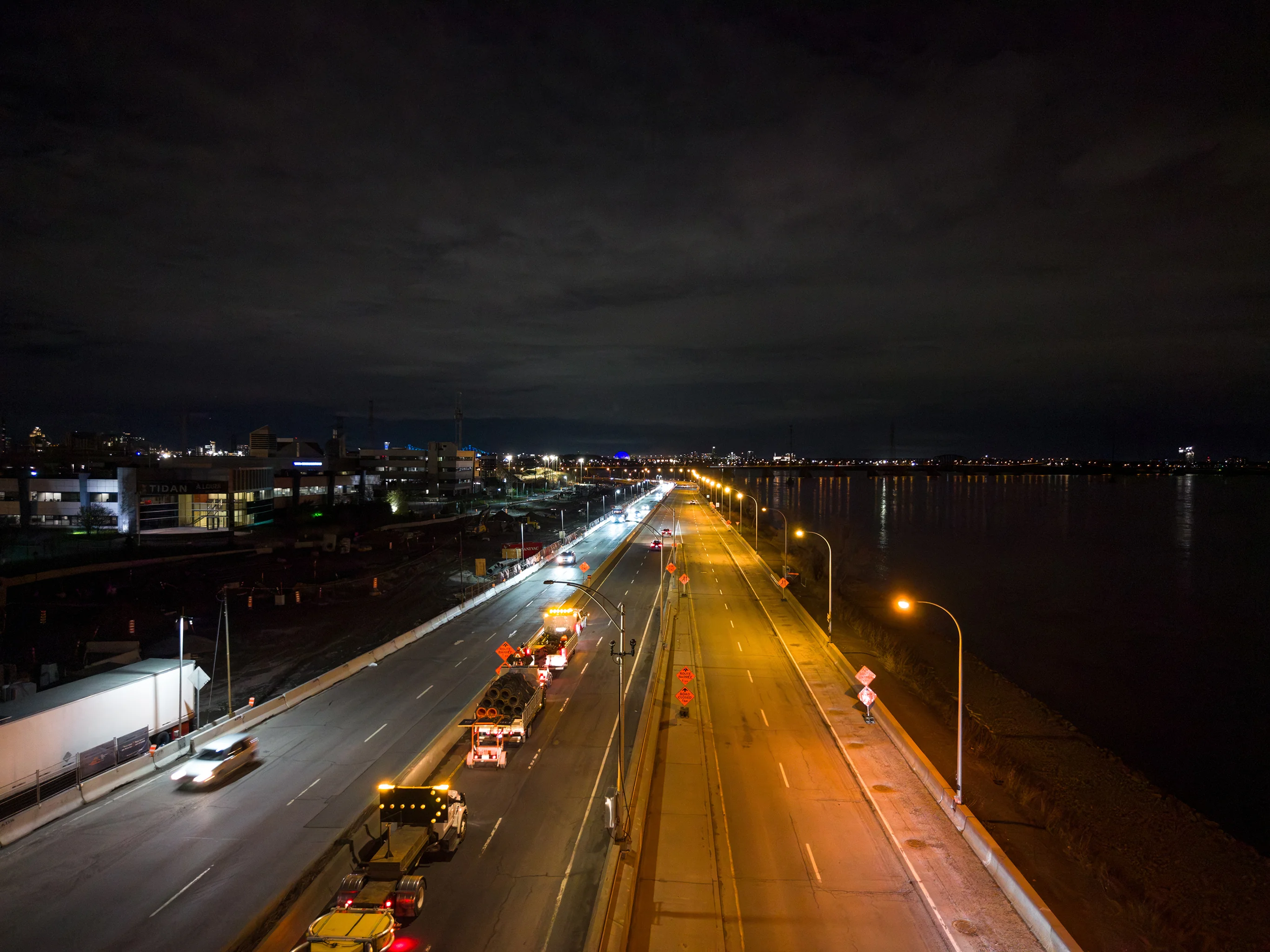 Vue aérienne nocturne d'un chantier Maestro sur l'autoroute Bonaventure, voie fermée et balises devant le skyline de Montréal.