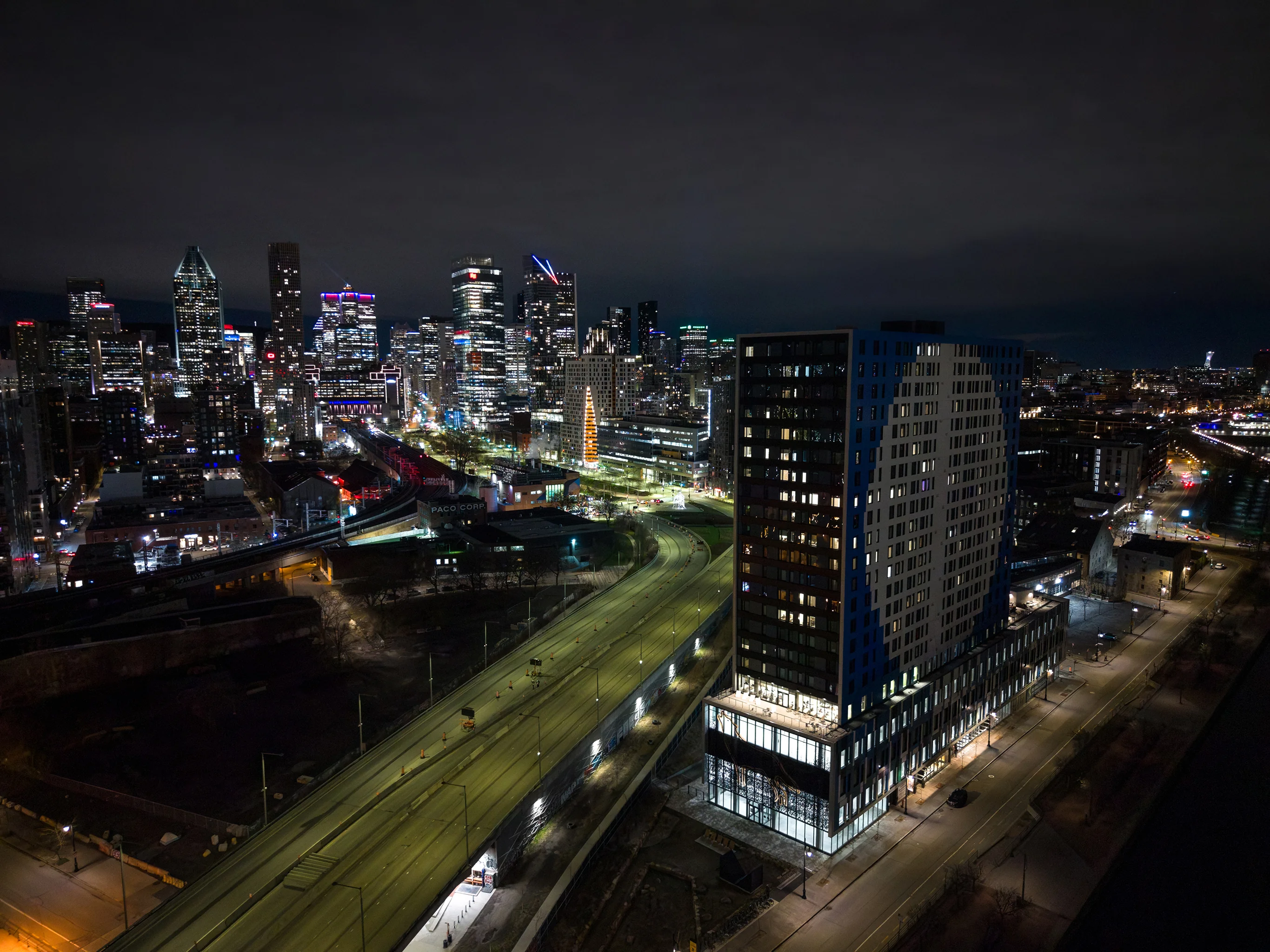Vue aérienne nocturne du corridor de l'autoroute Bonaventure devant le skyline de Montréal pendant les travaux de réfection.